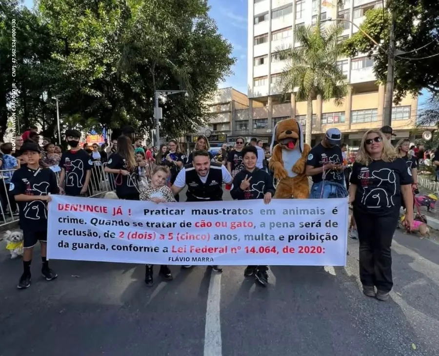 Participantes do Desfile Pet segurando faixa de conscientização contra maus-tratos a animais.